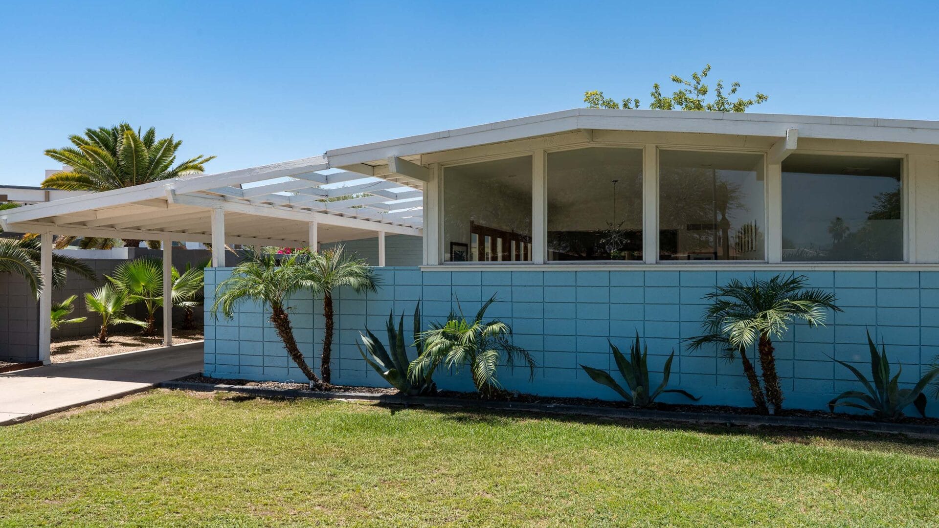 Front elevation of restored Ralph Haver home in Scottsdale featuring blue siding, white pergola structure, desert landscaping, and preserved mid-century modern architecture.