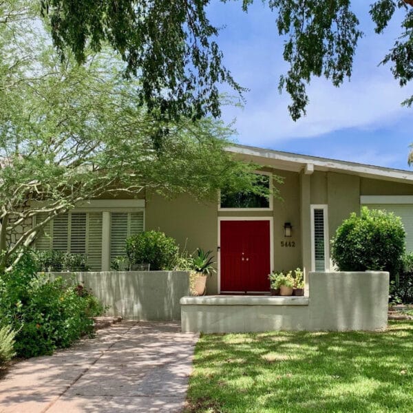 Mid-century modern home in Arcadia Phoenix with red front door, low roofline, stone accent wall, mature trees, lawn, and shaded landscaping.