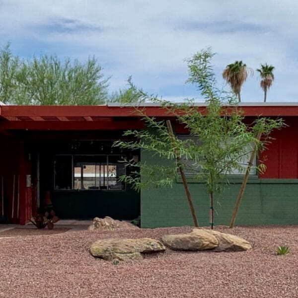 Mid-century modern home in Hy-View Scottsdale with red and green exterior, carport, low roofline, desert landscaping, and boulder accents.