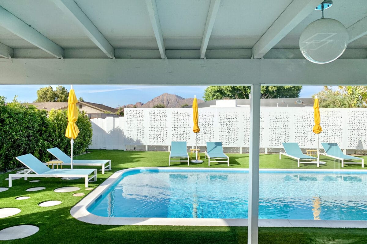 Sheridan rear patio and pool in Scottsdale with covered outdoor living area, breeze block wall, yellow umbrellas, pool, and mid-century modern landscape design.